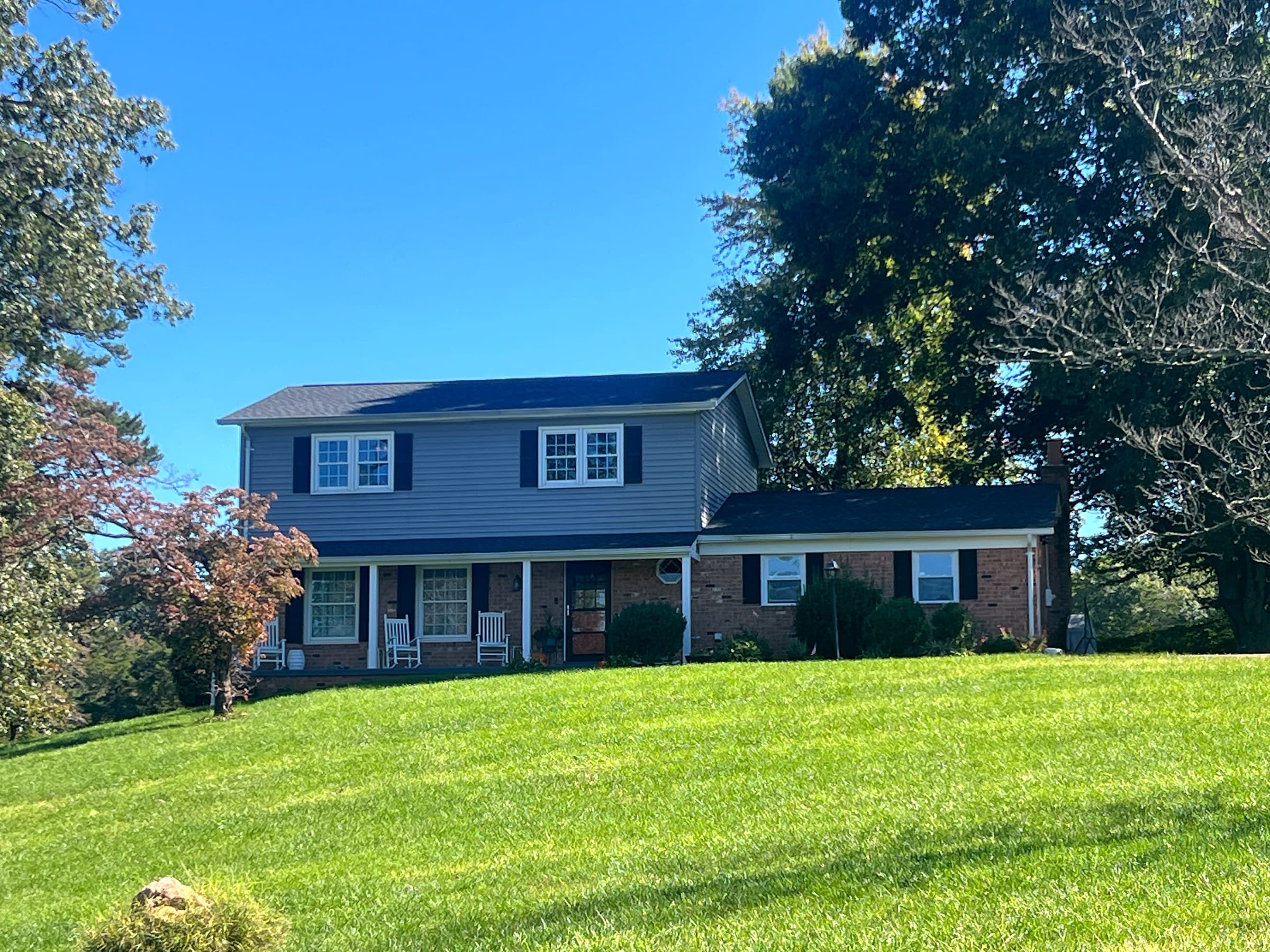 Two-story home in Culpeper, VA with a brick lower level, blue-gray siding, black shutters, a front porch with white rocking chairs, and a GAF Timberline HDZ Charcoal roof