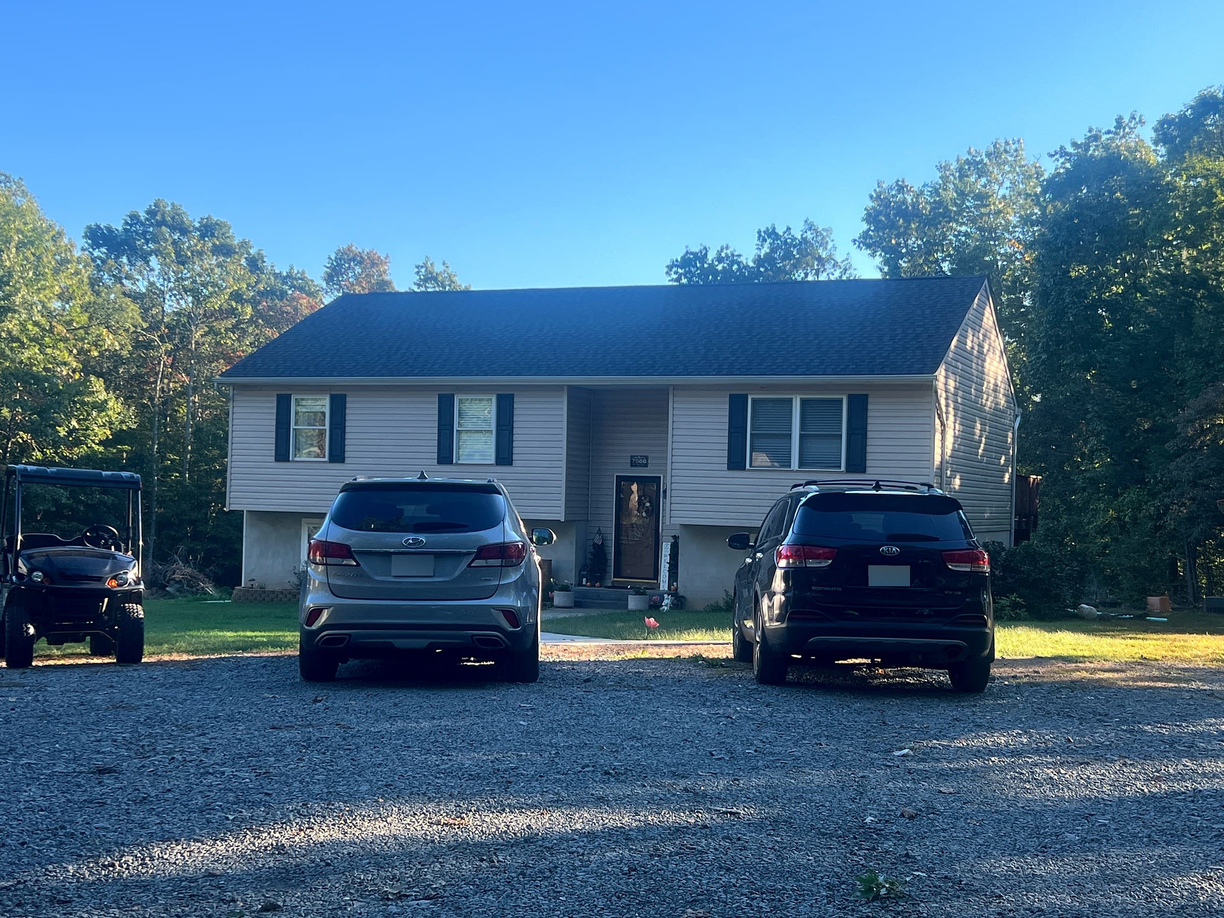 Split-foyer home in Culpeper, VA with beige siding, black shutters, a front door with a wreath, two SUVs and a utility vehicle in the gravel driveway, and a GAF Timberline HDZ Appalachian Sky roof
