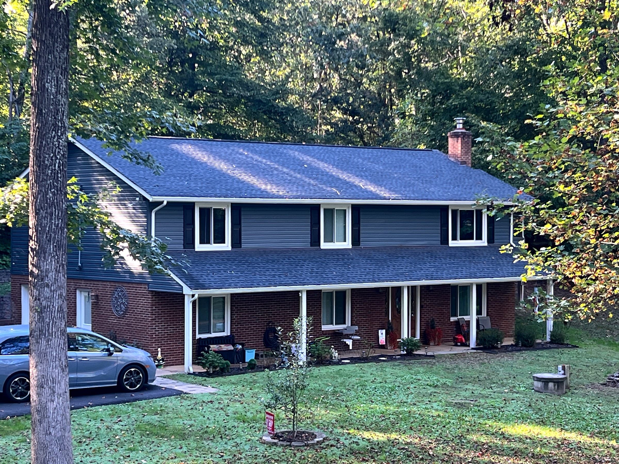 Two-story home in the Fredericksburg mailing area of Stafford County, with blue-gray siding, a long covered porch, a foreground tree, and a new GAF Timberline HDZ Charcoal roof.