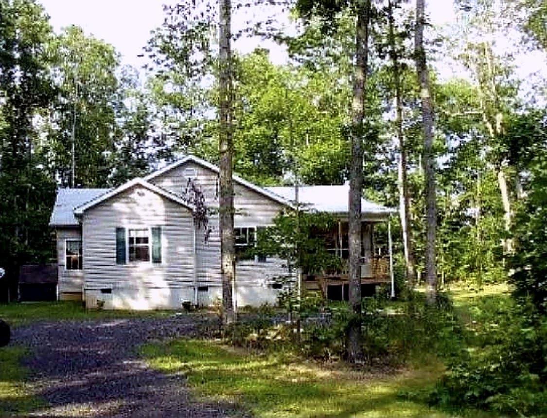 White ranch home in Rhoadesville, VA with an older dark asphalt roof, red shutters, a covered front porch, and a realtor watermark in the corner