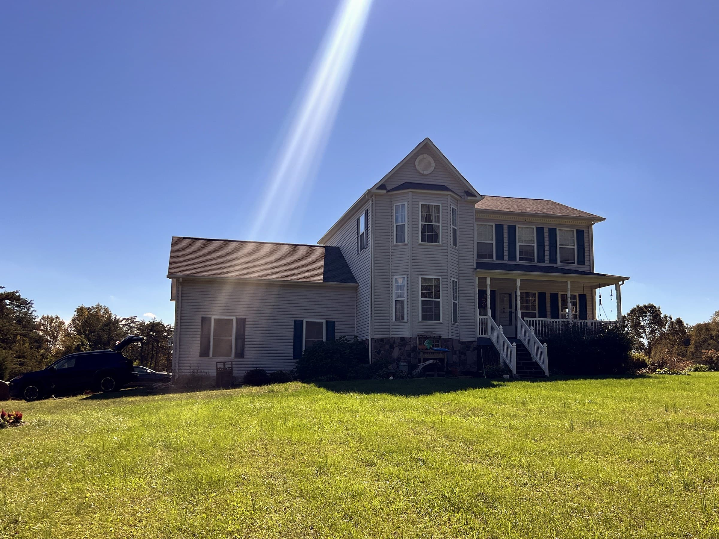 Two-story home in Rhoadesville, VA with a new GAF Timberline HDZ Slate roof, sun flare across the upper windows, and an SUV parked at the left