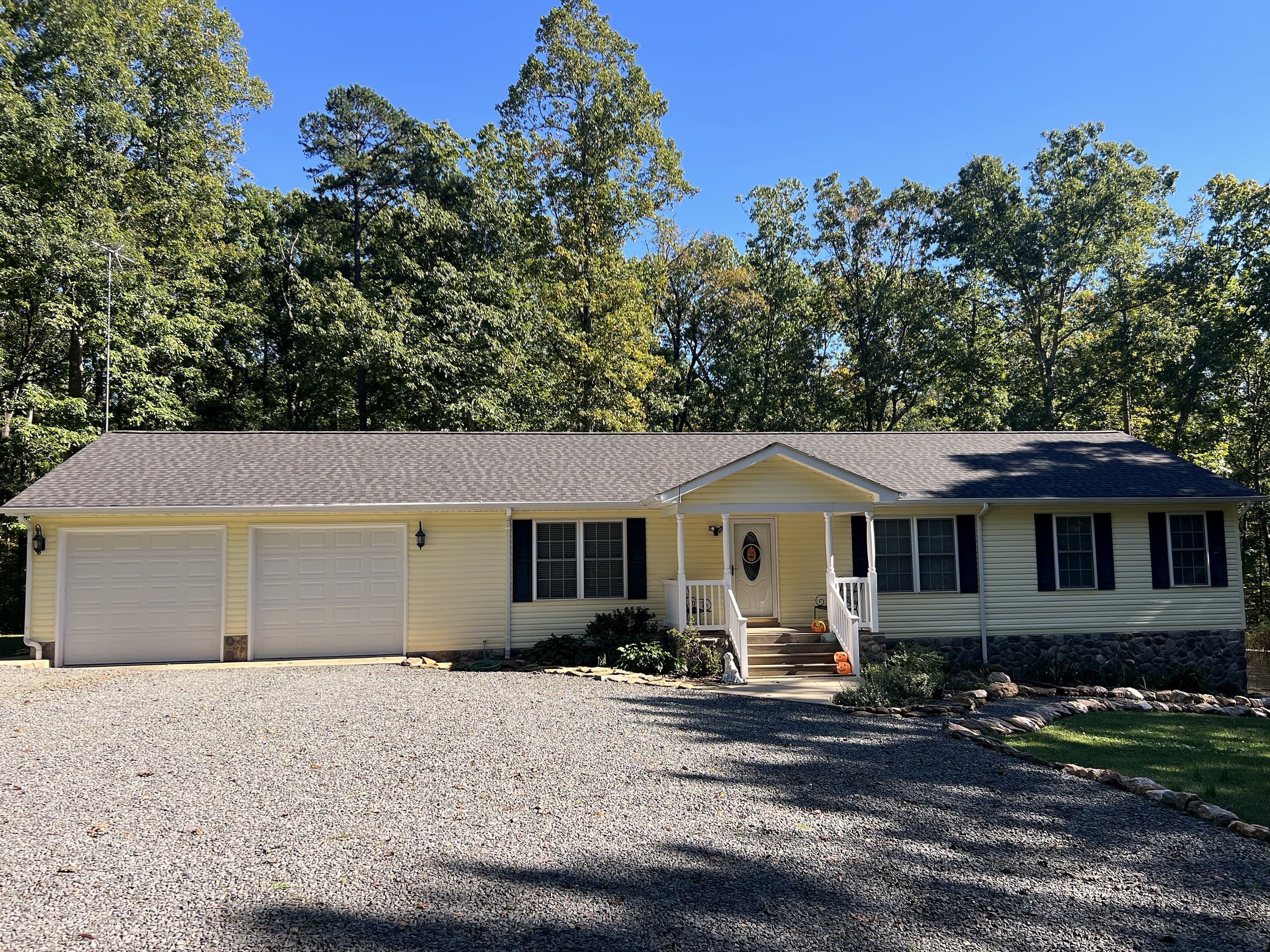 Pale yellow ranch home in Rhoadesville, VA with a new GAF Timberline HDZ Slate roof, two-car garage, stone foundation, and pumpkins by the garage