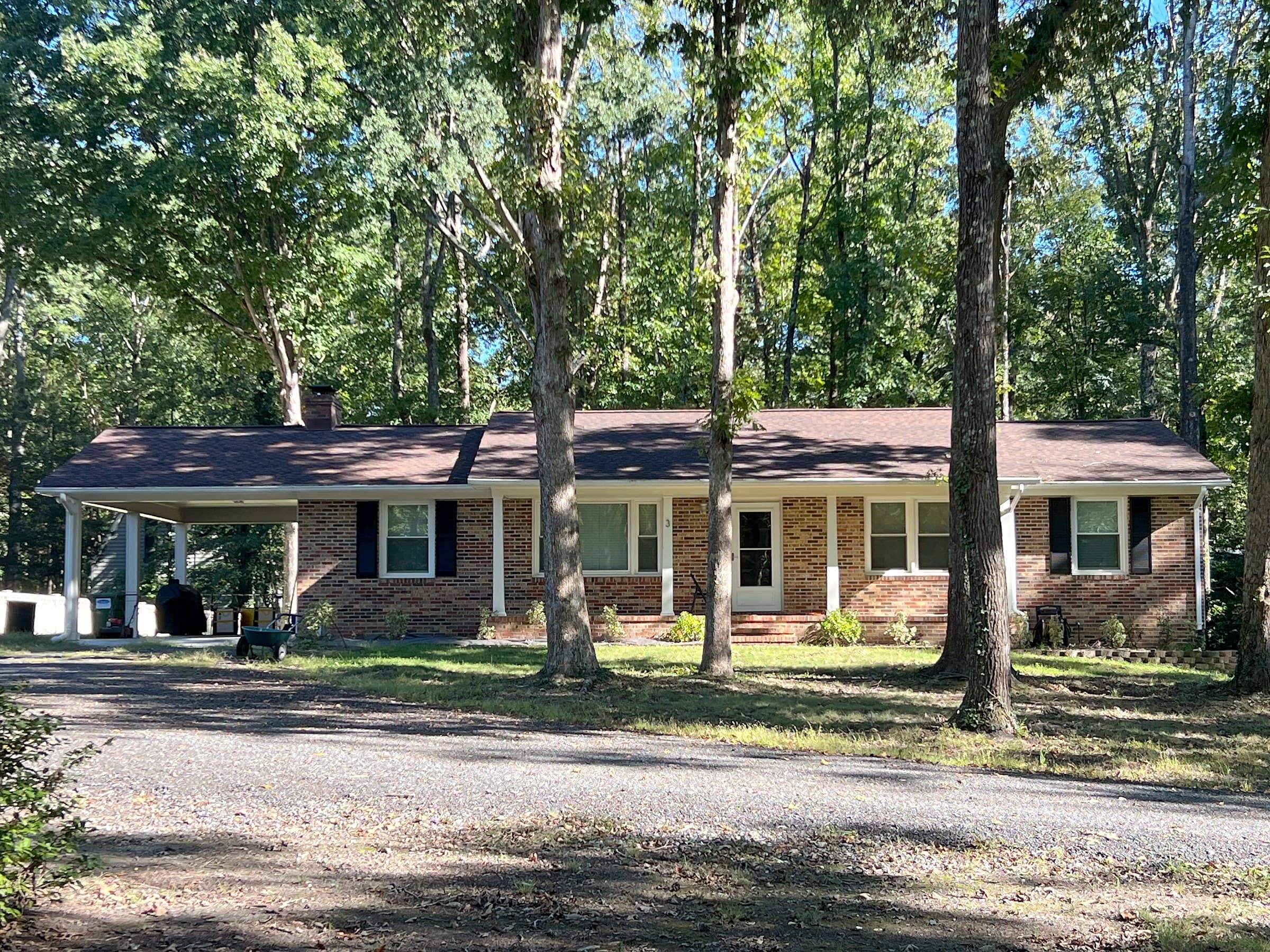 Brick ranch home in Falmouth, Stafford County, with an attached carport, black shutters, tall front-yard trees, and a new GAF Timberline HDZ Hickory roof.