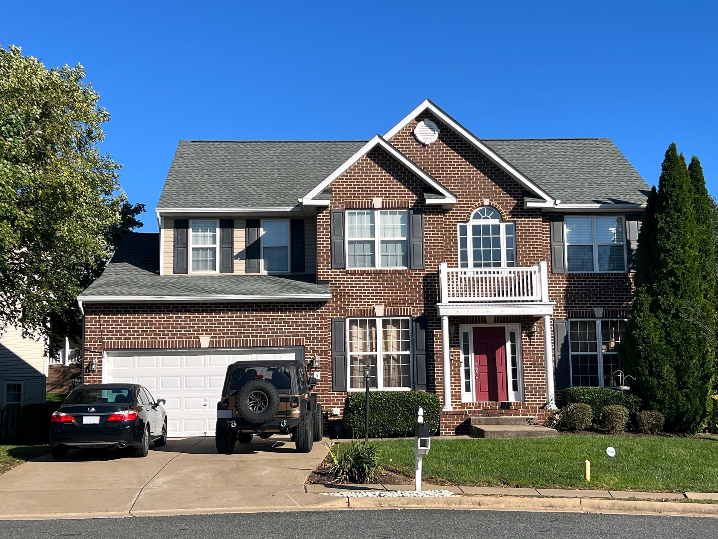 Two-story brick colonial in Leeland Station, Stafford County, with a red door, white balcony, two-car garage, and a new GAF Timberline HDZ Slate roof.